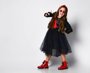Young positive plus size girl in bright rock style clothing, red boots and glasses standing and showing peace sign with fingers