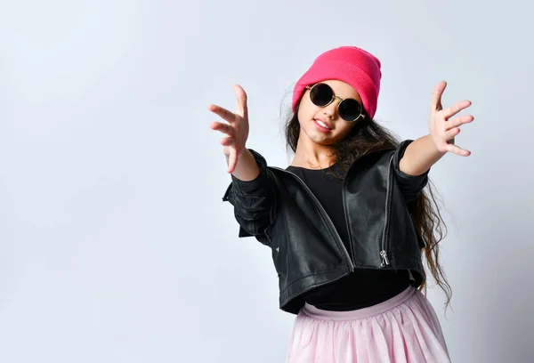 Дитина-підліток у шкіряній куртці, рожевому капелюсі та сонцезахисних окулярах. Вона посміхається, тягне до тебе руки, ізольовано на білому. крупним планом — стокове фото