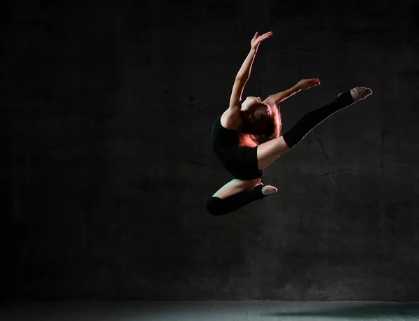 Молодая девушка гимнастка в черном спортивном теле и верхней делает круг в прыжке через темный фон с красочными блестящими — стоковое фото