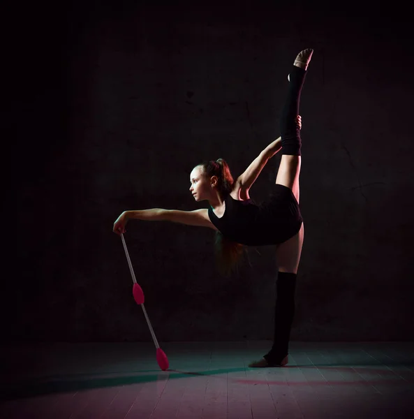 Jong lachend meisje turner in zwarte sport lichaam en bovendelen staan en houden twee roze gymnastiek maces in de hand — Stockfoto