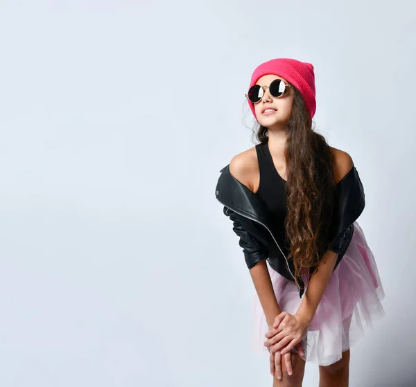 Adolescente em jaqueta de couro preto, saia, chapéu rosa e óculos de sol. Ela sorrindo enquanto posava em pé isolada no branco. Fechar — Fotografia de Stock