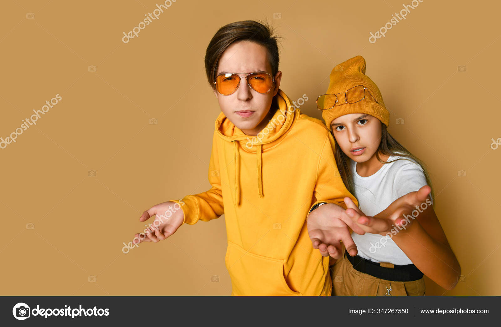 Young teens boy and girl in comfortable clothing, hats and sunglasses  standing and expressing misunderstanding — Stock Photo © ddkolos.gmail.com  #347267550