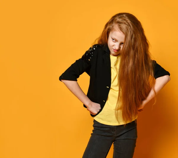 Teenage kid in black jacket and yellow t-shirt. She is looking pissed off, hands on hips, posing on orange background. Close up — Stock Photo, Image