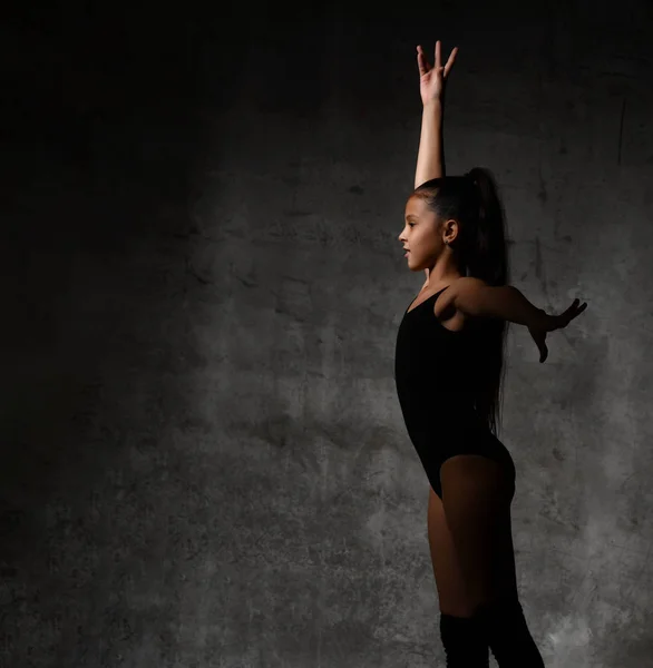 Siyah spor vücutlu genç bir jimnastikçi kız ve ayakta duran ve siyah arka planda jimnastik yapan özel jimnastikçiler. — Stok fotoğraf
