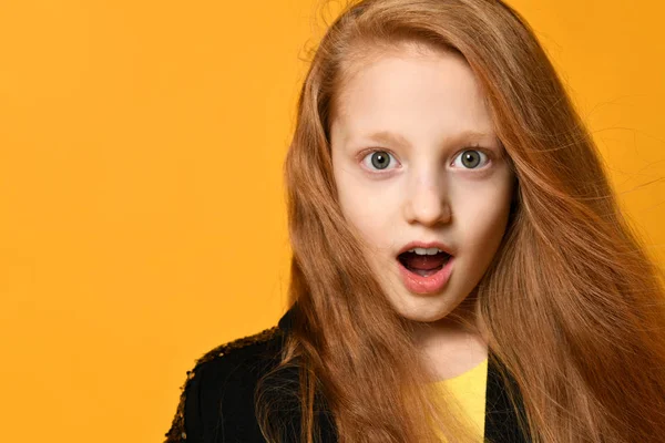 Roodharige tiener in zwart jasje en geel t-shirt. Ze kijkt verbaasd, poserend tegen een oranje achtergrond. Sluiten. — Stockfoto