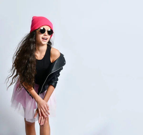 Adolescente em jaqueta de couro preto, saia, chapéu rosa e óculos de sol. Ela sorrindo enquanto posava em pé isolada no branco. Fechar — Fotografia de Stock