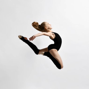 At kuyruklu esmer kız jimnastikçi, siyah taytlı, diz çoraplı, bale ayakkabılı, egzersiz yapan, beyazlara poz veren. Yakın plan..