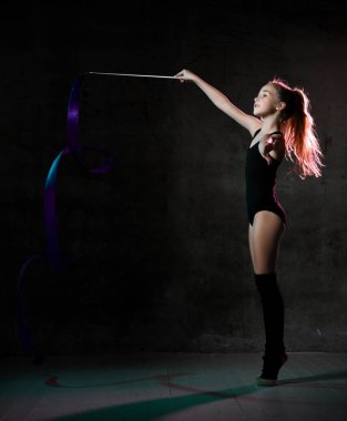 Siyah spor vücutlu genç bir jimnastikçi kız ve kenarda durup mavi jimnastik bandıyla egzersiz yapıyor.