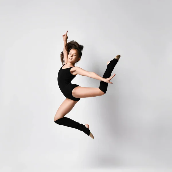 Ginnasta adolescente bruna con codino, in body nero, calze al ginocchio e scarpe da ballo, che esegue esercizi, posa isolata sul bianco. Primo piano . — Foto Stock