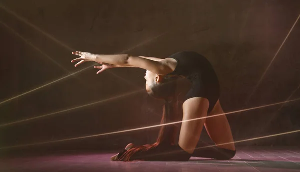 Giovane ginnasta ragazza in corpo nero sport e calzature speciali fare posa ginnastica su sfondo scuro — Foto Stock