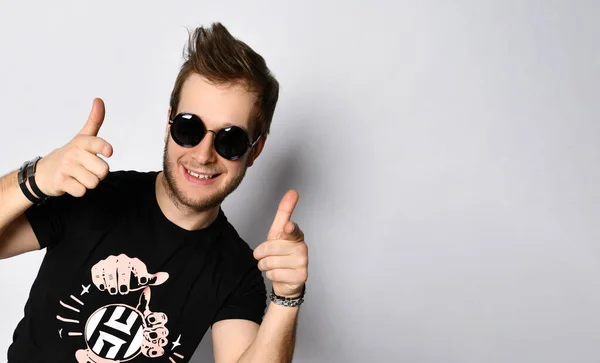 Homem de óculos de sol, t-shirt preta, pulseiras, jeans e ténis. Sorrindo, mostrando os polegares para cima posando isolado no branco. Comprimento total — Fotografia de Stock