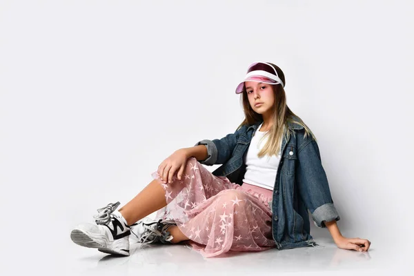 Jovem adolescente modelo de menina em roupas casuais elegantes e tênis sentado e olhando para a câmera sobre fundo branco — Fotografia de Stock