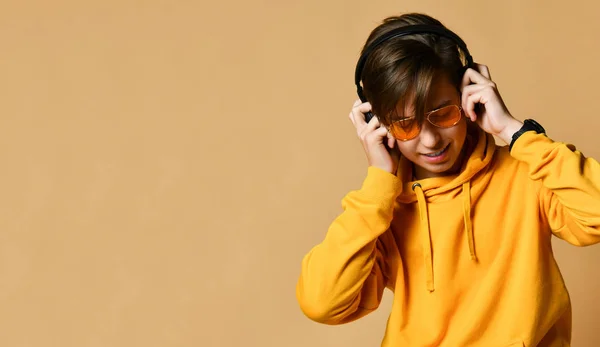 Young positive teen boy in yellow hoodie, sunglasses and headphones standing and smiling — Stok fotoğraf