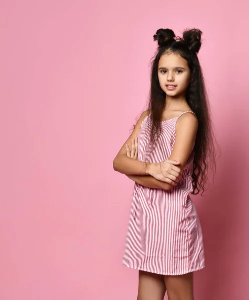 Teenage female with fancy hairstyle, in striped dress. She is smiling, posing with folded hands against pink background. Close up — Stok fotoğraf