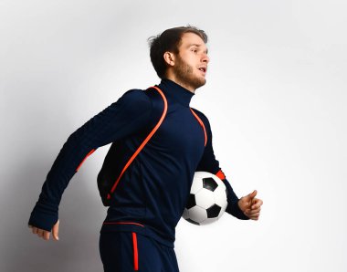 Mavi eşofmanlı ve sırt çantalı yetenekli erkek futbolcu koşuyor, elinde bir top, beyaz üzerinde yanlamasına poz veriyor. Kapat.