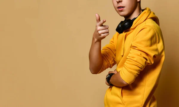 Νεαρό θετικό έφηβος αγόρι σε κίτρινο hoodie και ακουστικά στέκεται, χαμογελώντας και κοιτάζοντας κάμερα πάνω από κίτρινο φόντο τοίχο — Φωτογραφία Αρχείου