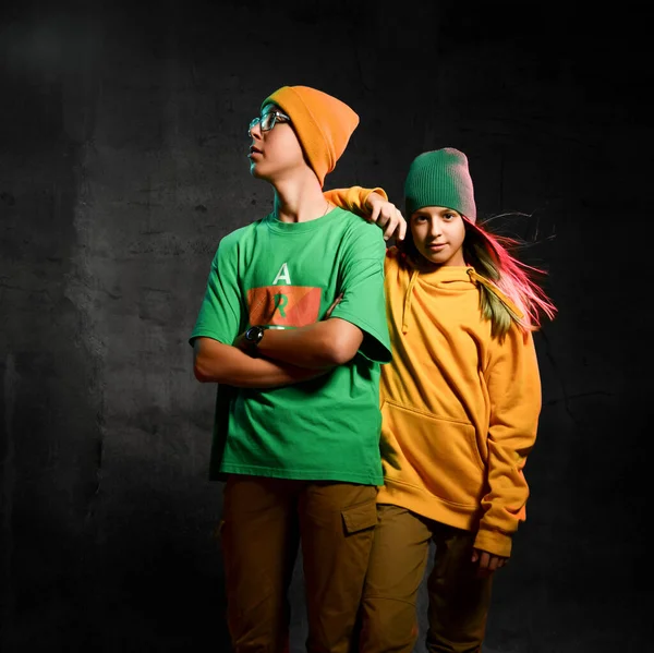 Adolescentes jóvenes niño y niña en verde y amarillo elegante ropa casual cómoda y sombreros de pie sobre fondo oscuro — Foto de Stock