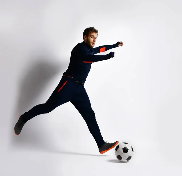 Jugador de fútbol experto en chándal azul y zapatillas de color. Está a punto de golpear la pelota, posando aislado sobre blanco. Longitud completa —  Fotos de Stock