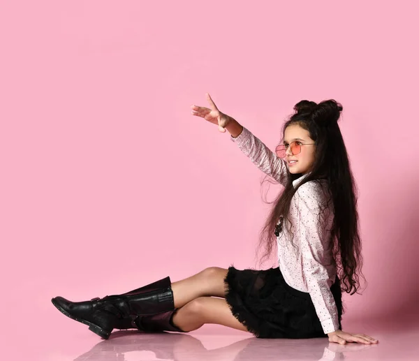 Niño adolescente con pelo largo, gafas de sol, blusa blanca, falda negra y botas. Posando sentado sobre un fondo rosa. De cerca. — Foto de Stock