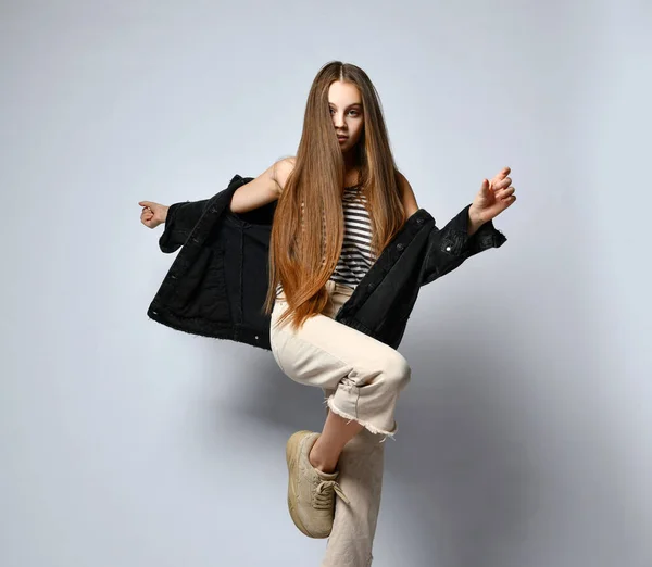 Adolescent in gestreept t-shirt, zwarte denim jas, broek en sneakers. Ze poseert geïsoleerd op een witte achtergrond. Sluiten. — Stockfoto