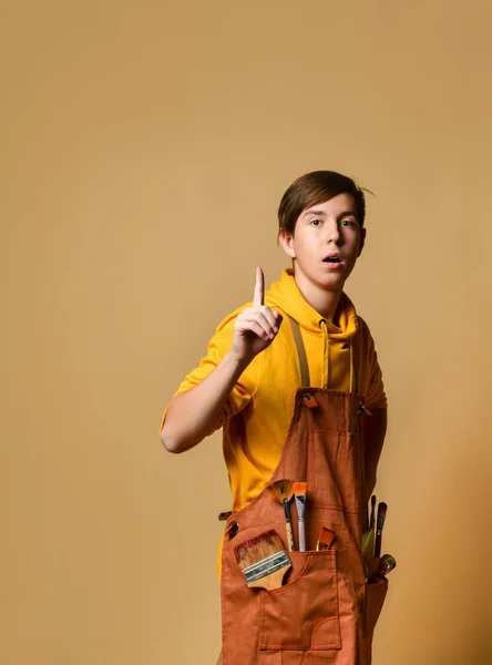 Jugendlicher Maler in gelbem Kapuzenpulli und Overall auf Staffelei vor gelbem Hintergrund — Stockfoto