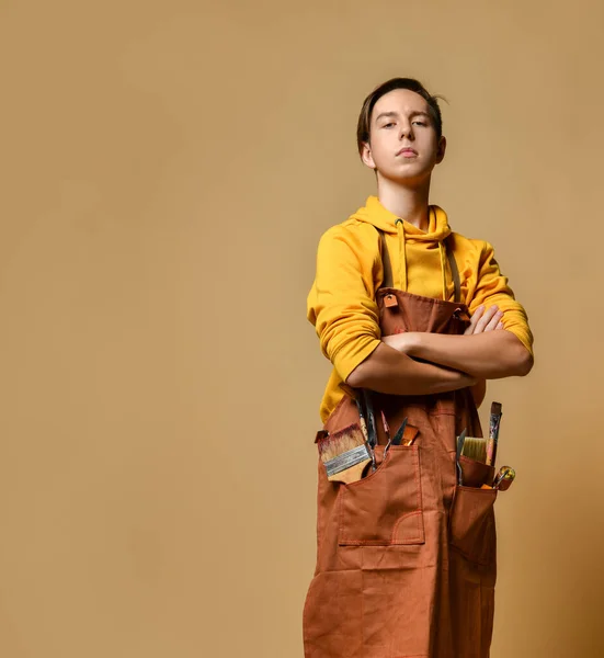 Νεαρός έφηβος ζωγράφος αγόρι σε κίτρινο hoodie και jumpsuit στέκεται στο καβαλέτο πάνω από κίτρινο φόντο — Φωτογραφία Αρχείου