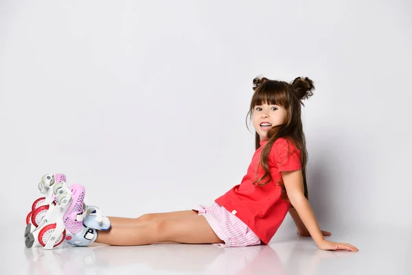 Menina bonita posando sentado no chão, em uma camiseta vermelha e shorts e um penteado elegante, em patins em seus pés — Fotografia de Stock