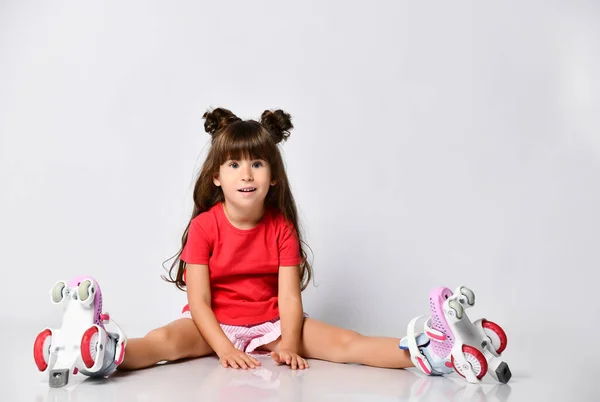Красивая девушка позирует сидя на полу, в красной футболке и шортах и модной прическе, в роликовых коньках на ногах — стоковое фото
