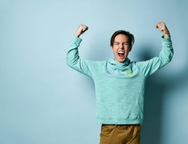 Mavi kapüşonlu genç çocuk ayakta, bağırıyor ve güçlü hissediyor..