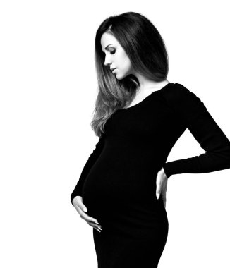 Dar elbiseli hamile bir kadının siyah beyaz fotoğrafı. Ellerini karnına koydu, beyaz arka planda izole bir şekilde poz verdi. Kapat.