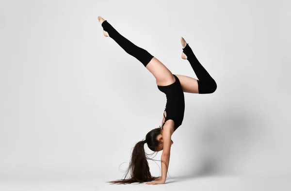 Gimnasta adolescente en maillot negro, calcetines de rodilla y zapatillas de ballet, realizando ejercicios de pie sobre sus manos, boca abajo, aislada en blanco. Primer plano — Foto de Stock