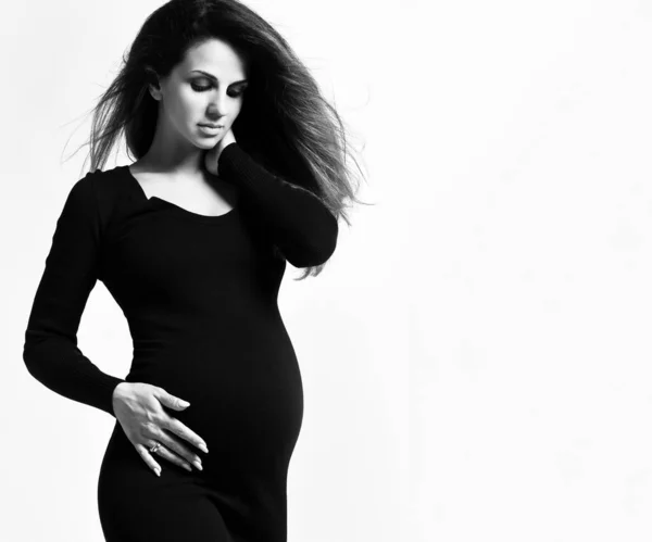 Black and white photo of pregnant female in tight dress. She put hands on her belly, posing isolated on white background. Close up — Stock Photo, Image