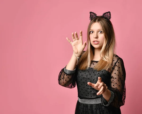 Teen girl in black dress, headband in form of cat ears, bracelet. Acting like she is a pussy, posing on pink background. Close up — Stok fotoğraf