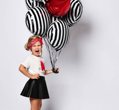 Kırmızı saç bandı takmış, beyaz tişörtlü küçük şirin bir kız elinde bir sürü balon tutuyor.