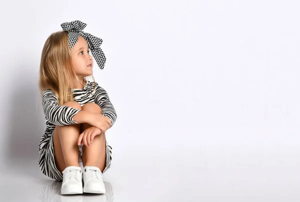 Studio schoot klein meisje in een gestreepte jurk en haarband. Zit op de vloer en kijkt naar de plaats voor uw advertentie — Stockfoto