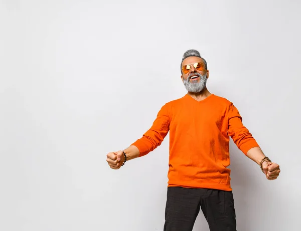 Hombre mayor en jersey naranja, gafas de sol, pantalones negros, pulseras. Puños levantados, gritando, posando aislados sobre blanco. De cerca. — Foto de Stock
