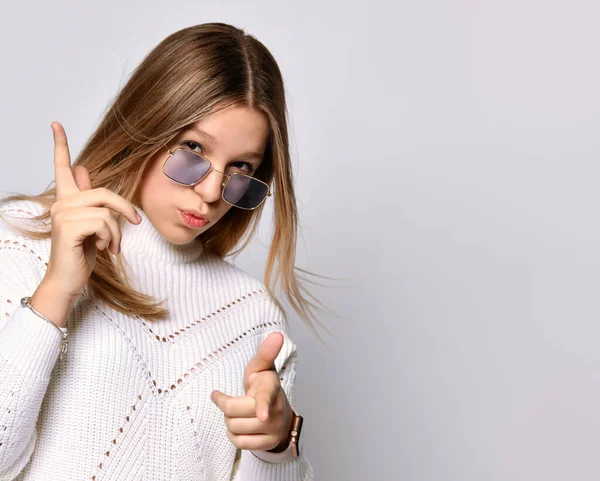 Ragazza adolescente bionda in occhiali da sole, orologio intelligente, braccialetto e maglione. Ti sta indicando, posa isolata sul bianco. Da vicino. — Foto Stock