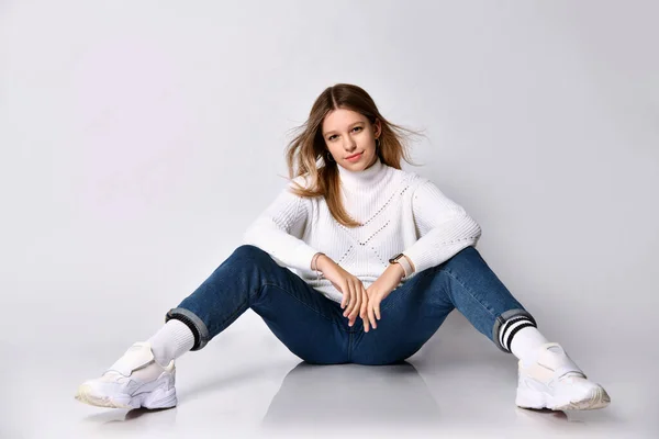 Mulher adolescente de jeans, camisola, meias e tênis. Sorrindo, sentado no chão, pernas afastadas, isolado em branco. Fechar — Fotografia de Stock