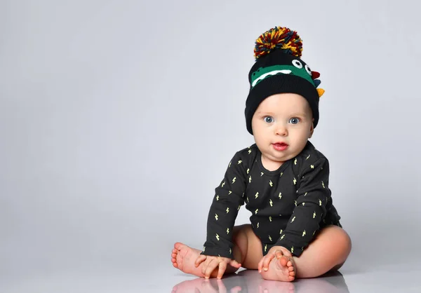 Baby boy in black bodysuit and hat with croco print, barefoot. He sitting on floor isolated on white studio background. Close up — Stock Photo, Image