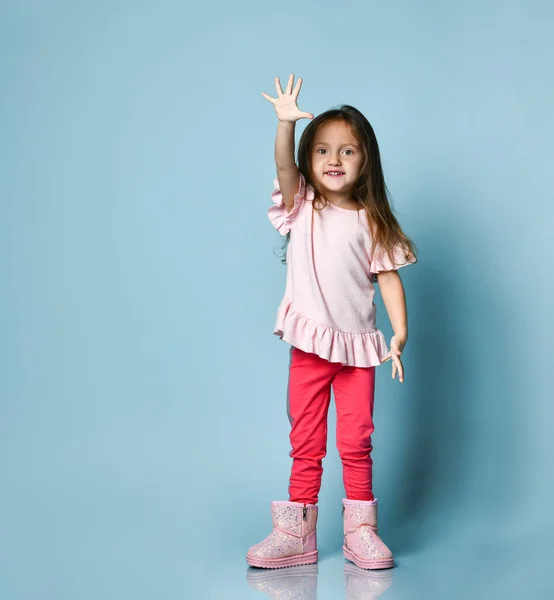 Klein blond meisje gekleed in roze blouse, broek en laarzen. Ze poseert tegen een blauwe studio achtergrond. Volledige lengte, kopieerruimte — Stockfoto