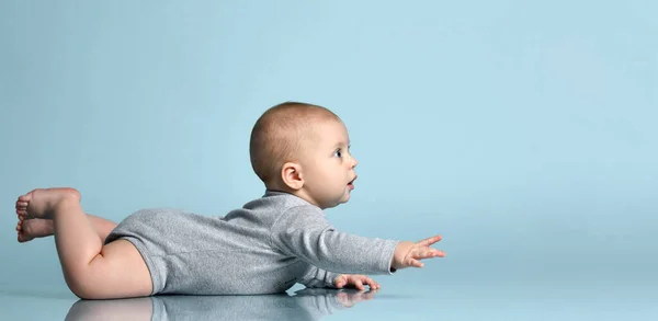 Ginger toddler in gray bodysuit, barefoot. He is sitting on the floor against blue studio background. Close up, copy space — Stock Photo, Image