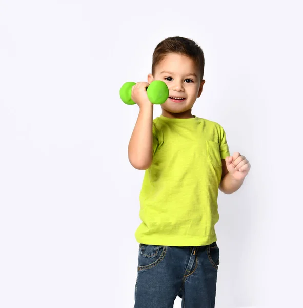 Little male in yellow t-shirt and denim shorts. He smiling, lifting green dumbbell, posing isolated on white studio background — Stock Photo, Image