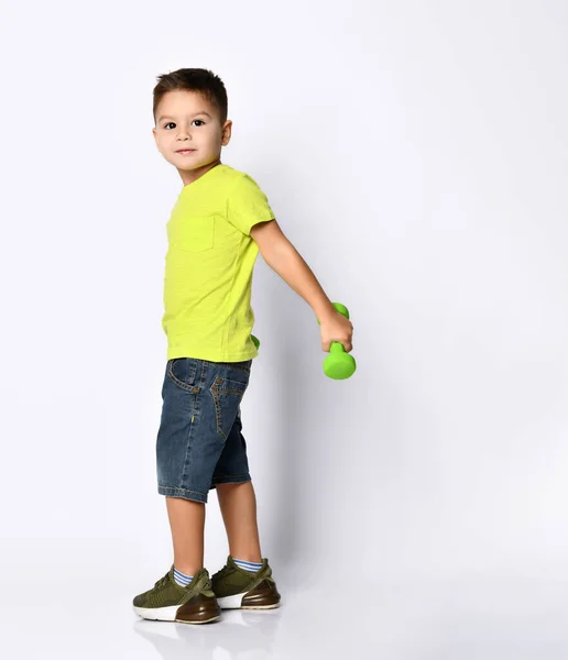 Sarı tişörtlü, kot şortlu, haki ayakkabılı küçük bir çocuk. Gülümseyen, yeşil dambıllar tutan, beyaz poz veren — Stok fotoğraf