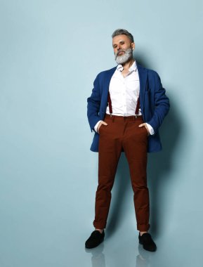 Beyaz gömlekli, ceketli, kahverengi pantolonlu, siyah ayakkabılı bir adam. Güneş gözlüklerini düzeltiyorum, el ele verip, mavi arka planda poz veriyorum.