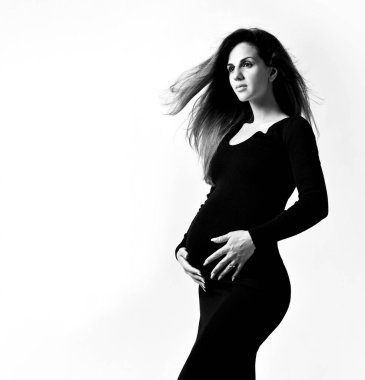 Siyah dar elbiseli esmer hamile kadın. O, beyaz üzerinde yanlamasına poz verirken elini karnının üzerine koydu. Kapat.