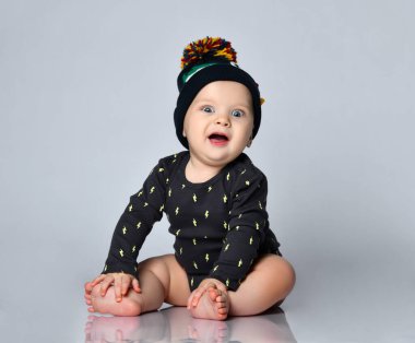 Baby boy in black bodysuit and hat with croco print, barefoot. He sitting on floor isolated on white studio background. Close up clipart