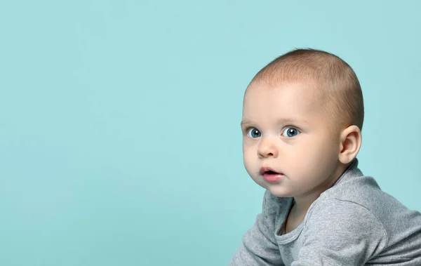 Porträtt av en baby i en grå bodysuit på en blå studio bakgrund. Begreppet artiklar om barndom eller reklam för barn. — Stockfoto