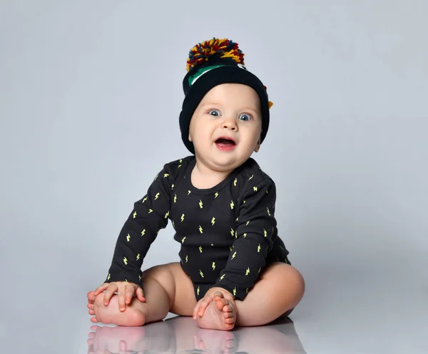 Baby pojke i svart body suit och hatt med krokodiltryck, barfota. Han sitter på golvet isolerad på vit studio bakgrund. Närbild — Stockfoto