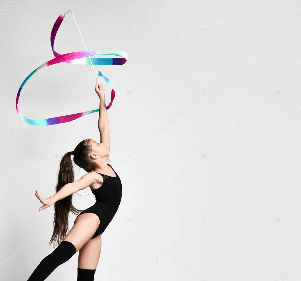 portrait of young brunette woman gymnast training calisthenics exercise with color ribbon on white studio background. Art gymnastics concept.
