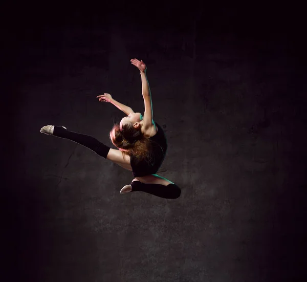 Giovane ginnasta ragazza in corpo nero sport e tomaie facendo cerchio in salto su sfondo scuro con scintillante colorato — Foto Stock